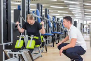 Fitnesstrainer unterstützt Mitglied beim Training